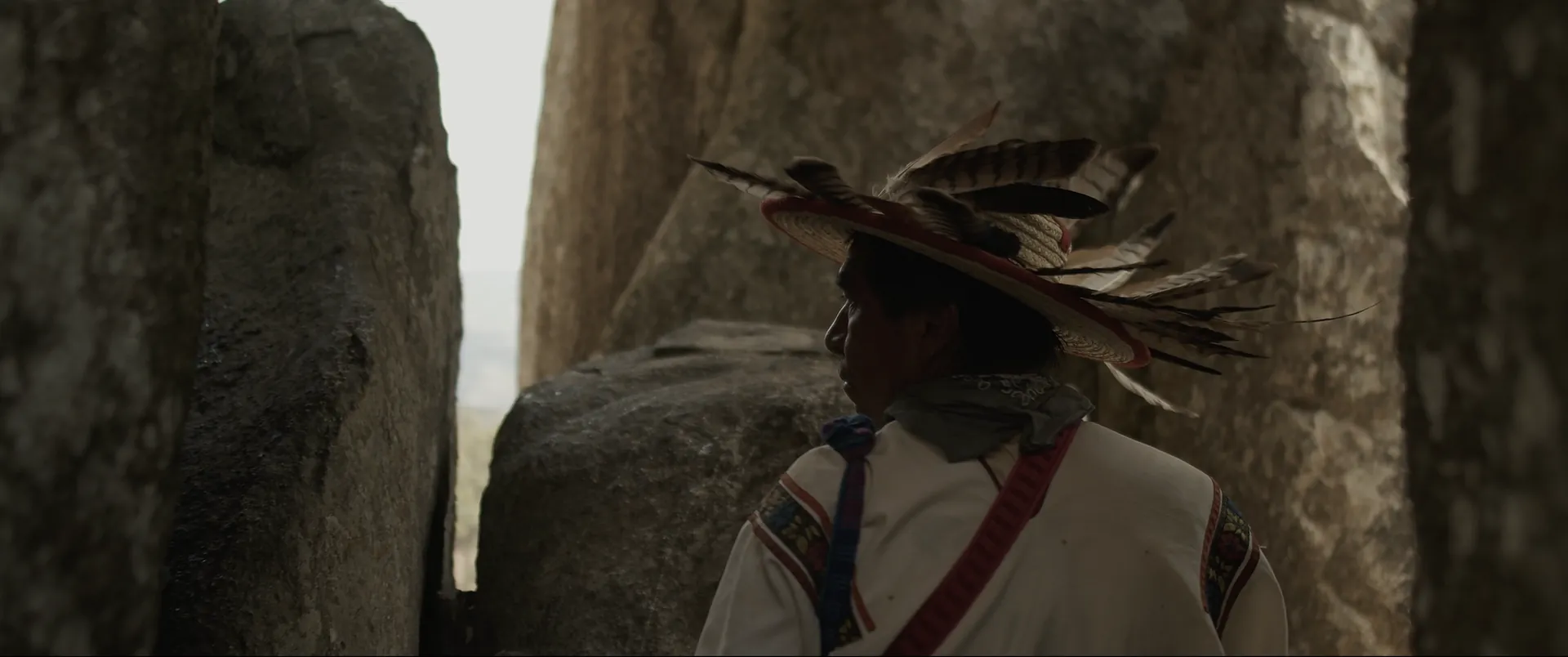 A Wixárika man in a feathered hat between standing stones