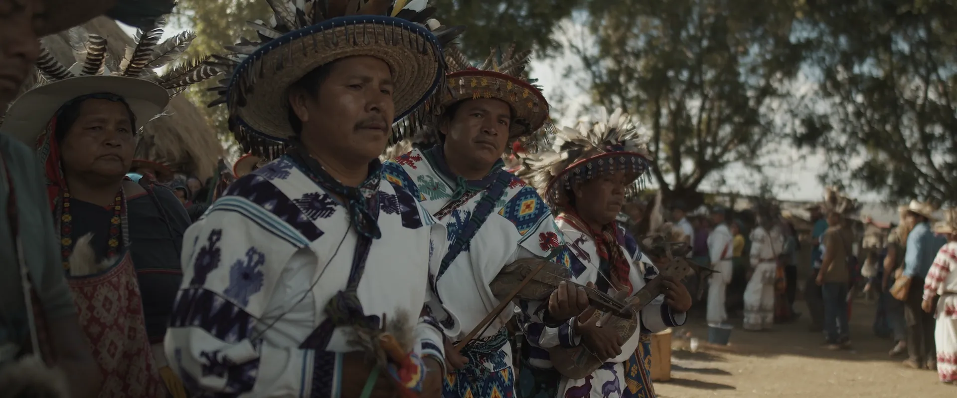 Wixárika elders in embroidered clothing and feathered hats at a gathering