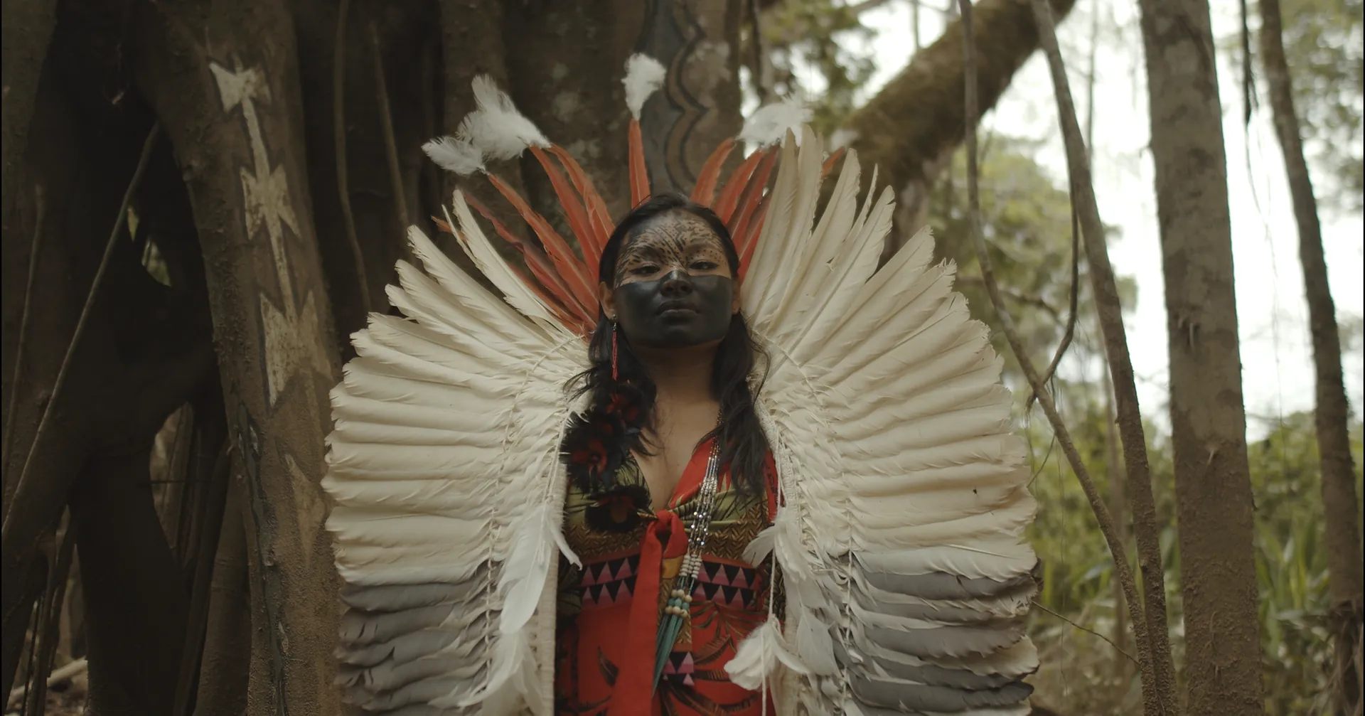 Woman in a white feather headdress and face paint standing in the forest