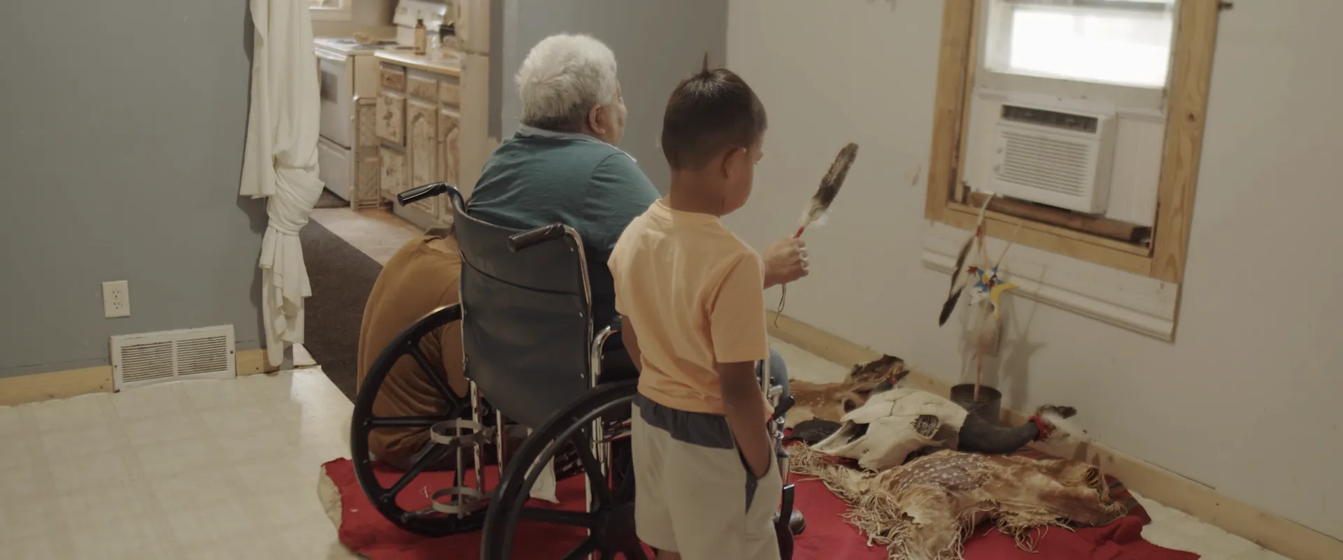 An elder in a wheelchair and a young boy looking at ceremonial items